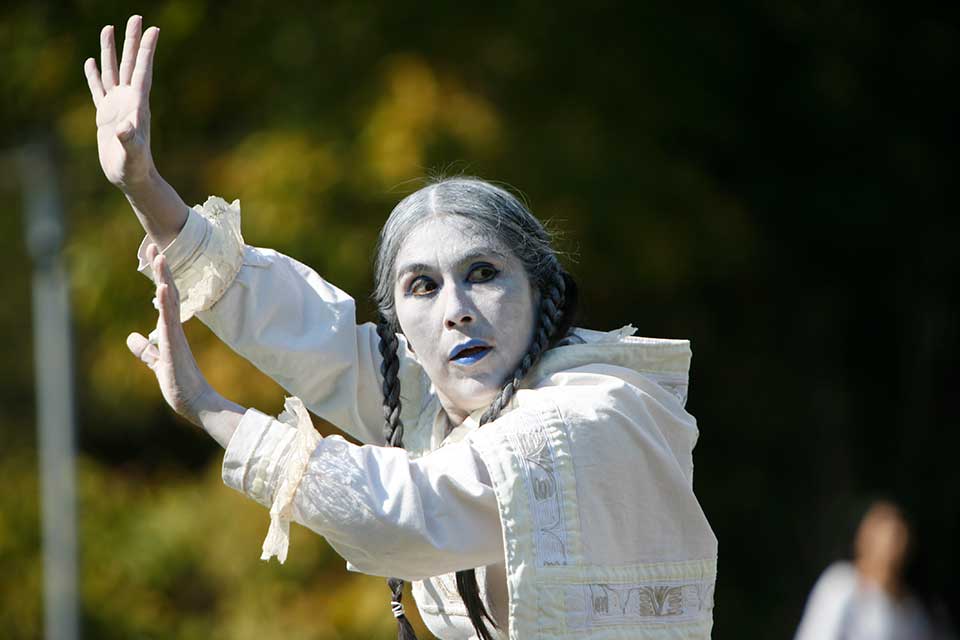 A performance artist puts their hands in the air and looks to the side