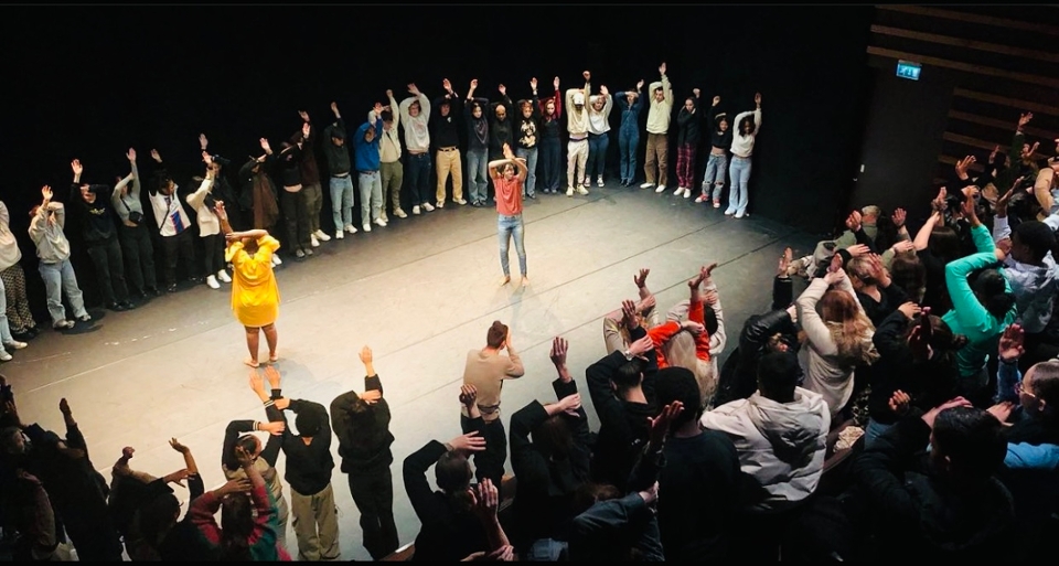 people standing in a circle on the stage with arms lifted up