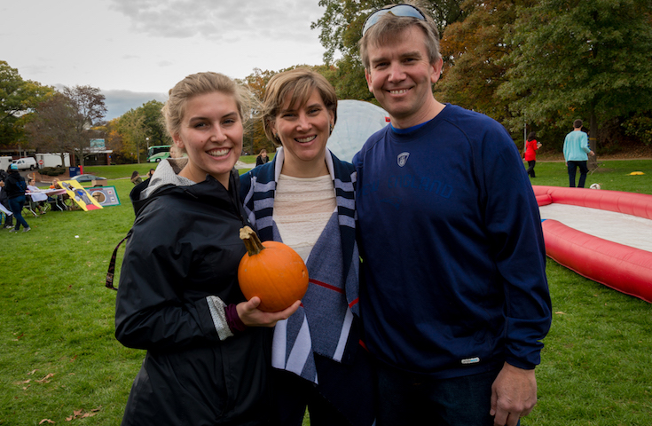 Two parents and college aged daughter holding a pumpkin