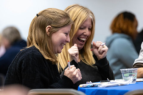 Two women laugh together while playing bingo at a table