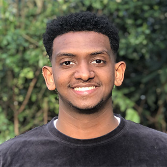 Mesoud Awol smiling in front of a tree