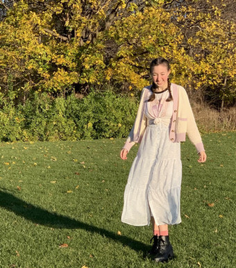 Emma stands outside, smiling, in a white dress.