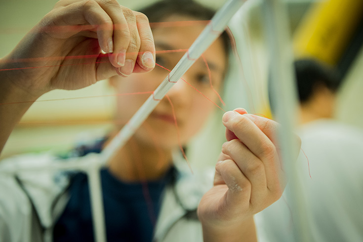 Student artist wrapping red string around a wooden dowel