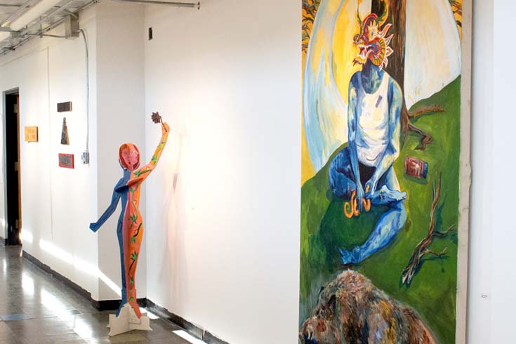 Installation shot in the halls of Goldman Schwartz; large painting in the foreground; sculpture of figure in the middle; small wood art pieces are in the background