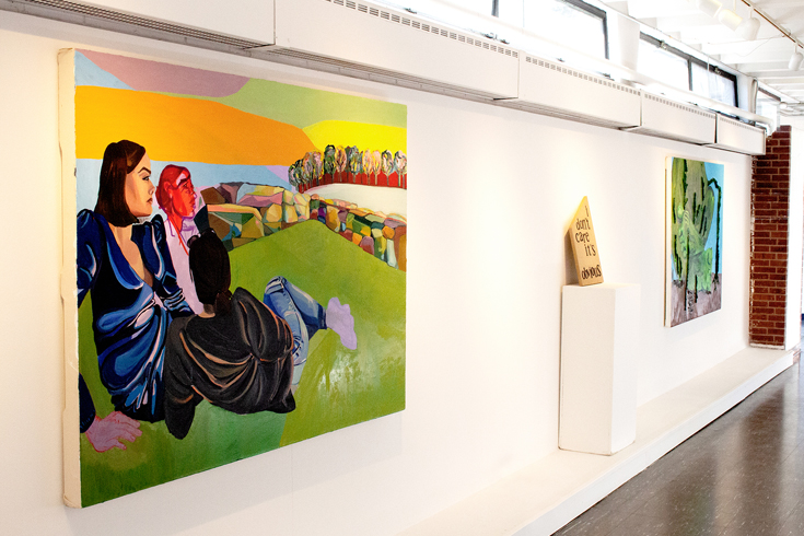 Two paintings and one sculpture are alongside a wall in a hallway.