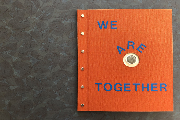An orange cover of a handmade book, text reads "We Belong Together"
