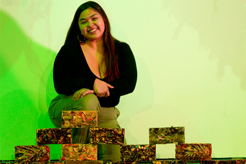 Zoila Coc-Chang kneels behind her rectangular sculptures in front of a neon green background