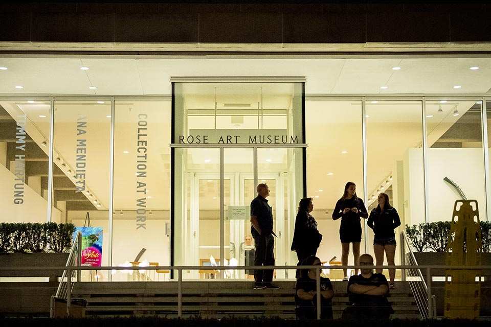 Exterior of Rose Art Museum lit up at night with silhouettes of visitors