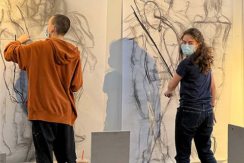 Schneider and Troupe working on humanlike figure drawings on large pieces of paper on the wall
