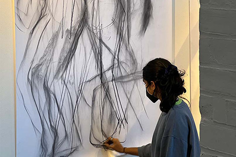 Rear view of Sequeira working on a large drawing of multiple and overlapping humanlike figures