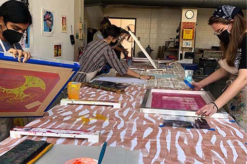 Sequira and Young screenprinting with other students working in the background