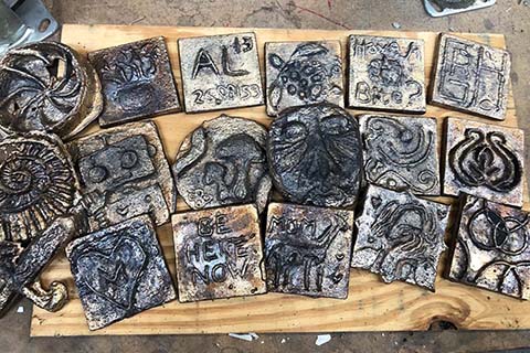 collection of 18 mainly square bronze casts varying in design laying on a piece of wood