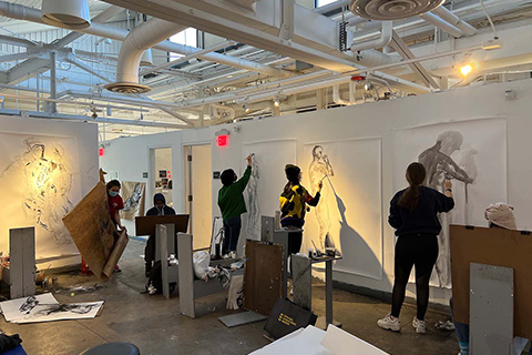 five students working on black and white art pieces of humanlike figures on large pieces of paper hung on the wall