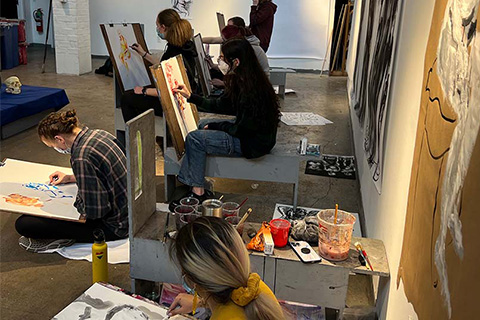 Collection of students working on both colorful and black and white drawings on paper while sitting