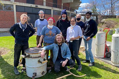 group of students and instructors smiling in front of the bronze pour can outside