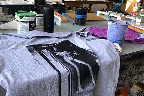 a screenprinted gray t shirt is in the focal point with two students working in the background
