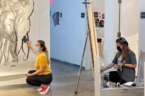 Young and Bucu crouching on the ground working on large drawings 