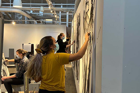 Side view of Bucu drawing on a paper with two students in the background