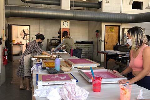 Bucu screen printing in pink with two others screen printing in the background
