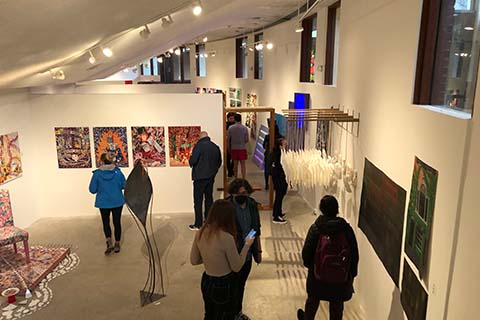 wide view of groups of students standing in a room looking at the artwork on the wall and chatting