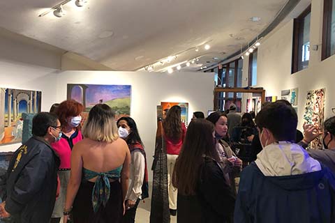 wide view of groups of students standing in a room looking at the artwork on the wall and chatting
