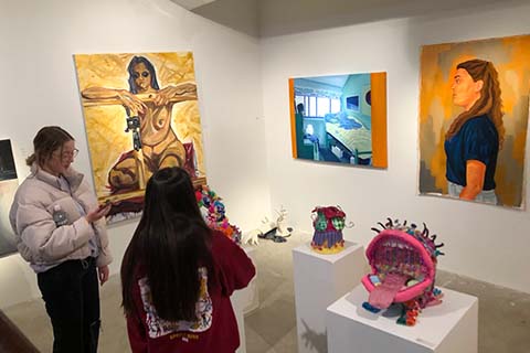 two students talking and looking at artwork on the wall and sculptures on pedestals