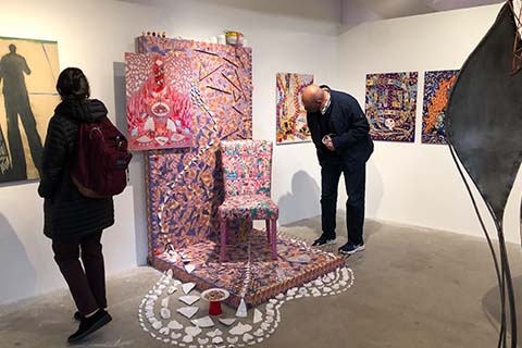 two people looking at artwork by Vicente Cayuela Aliaga on the wall and a pink sculpture of a chair with broken ceramic