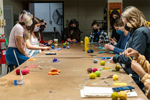 group of students surroundings a table with different color yarn spread out on the table