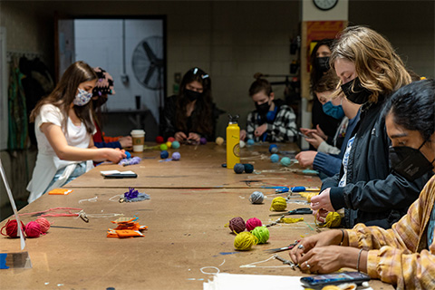 group of students surroundings a table with different color yarn spread out on the table