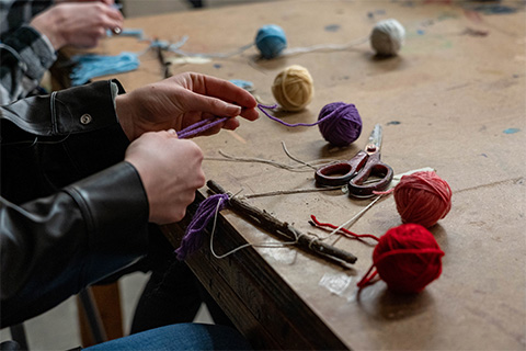 up close view of hands holding purple yarn, with other yarn balls surrounding it on a table