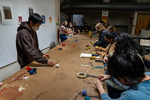 group of students surroundings a table with different color yarn spread out on the table