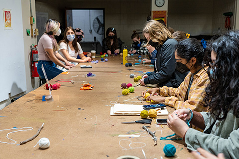 group of students surroundings a table with different color yarn spread out on the table