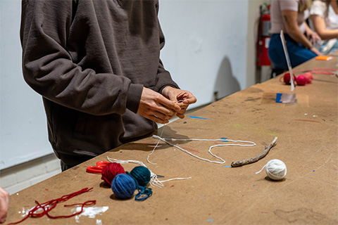 up close view of hands holding purple yarn, with other yarn balls surrounding it on a table