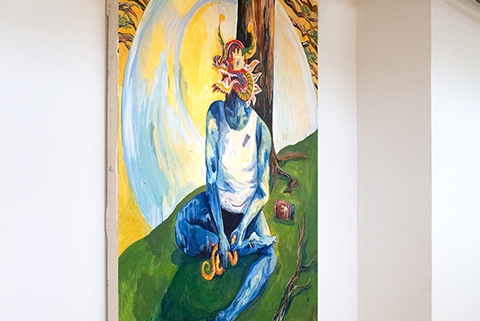 A nine-foot tall by four-foot wide landscape painting of a blue human wearing a dragon mask. The human is sitting under a tree holding a snake and there is a boar in the foreground.