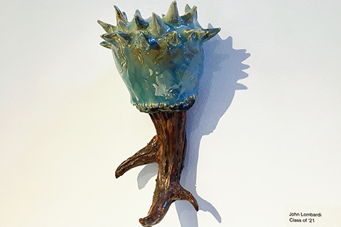 A twelve-inch tall by four-inch wide ceramic hanging sculpture of an organic form. The top half is green, spikey, and looks like some kind of vegetation. The bottom half is brown, looks like deer antlers, though in this context reads as roots.