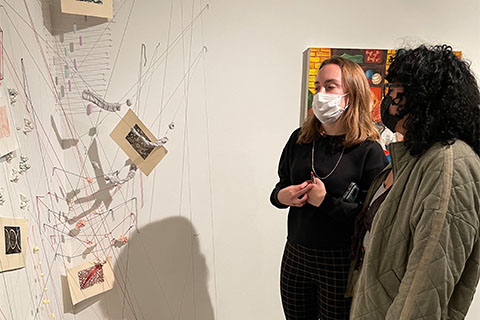 Maggie Moran and a student standing in front of Moran's piece. Pieces of paper attached by string with blobs on the ground holding the string down