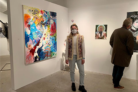 Leah Nashel standing in front of Nashel's art piece; bright colors layered on top of canvas