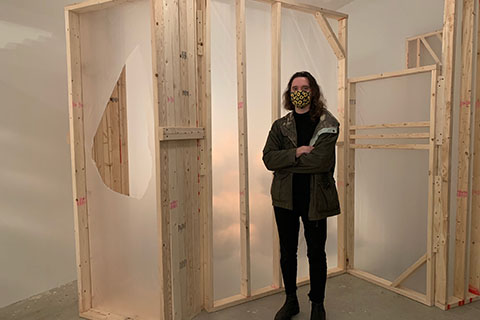 Liam Coughlin standing with arms crossed in front of a wood and plastic installation