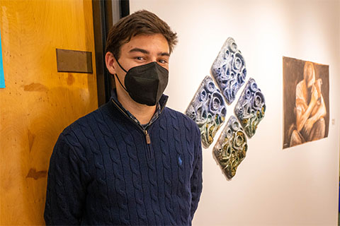 Ethan Frankel standing in front of Frankel's sculpture of four diamonds molded and painted in an ombre of white to green