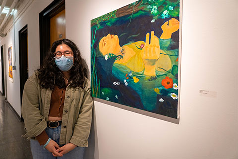 Norah Khadraoui standing in front of Khadraoui's painting of a woman half submerged in water surrounded by flowers and grass