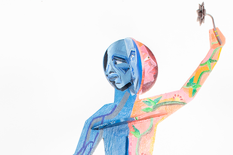 Plywood statue of a womanly figure with two faces. Three inserts in the head, chest, and legs. There is a blue male half, with a somber and serious expression. Deep blue veins running down the body. There is a pink female half, bright green vines and leaves running up the body, leading to a 3D printed flower. The pink woman gazes at the flower, with a content expression. Meant to evoke feelings of spring, hope, and growth.