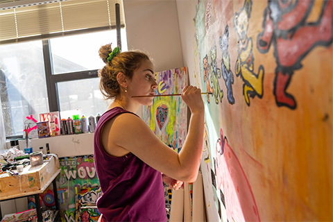 Side view of Rogers painting colorful bears on a canvas on the wall