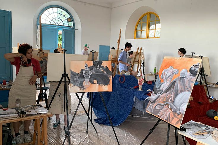 students stand in front of easels with paintings on them in an art studio in Siena, Italy