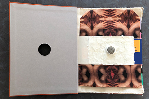 The first page is artist Tory Fair. The page is a horizontal strip because it is smaller than the dimensions of the book and some of the following pages. There is a white paper mache form protruding upward like a mini-volcano to expose a round river stone. This stone was seen through the hole in the cover of the book.