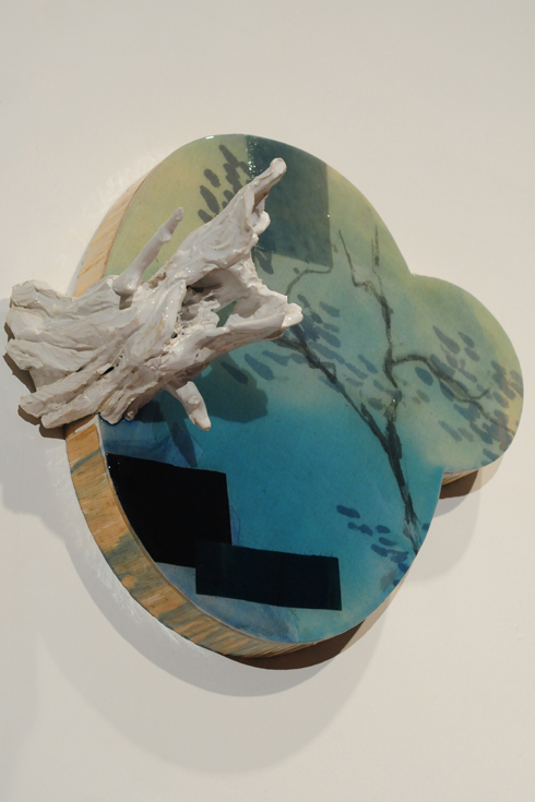 wood piece painted with hues of green and blue; tree branch painted white is attached to the side