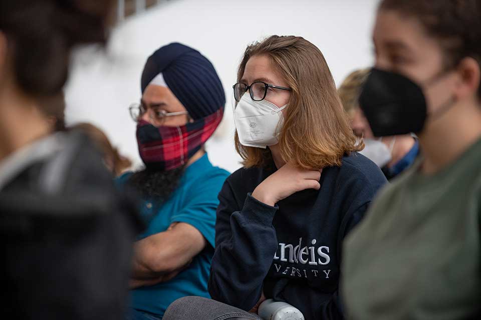 People wearing masks listen to a speaker