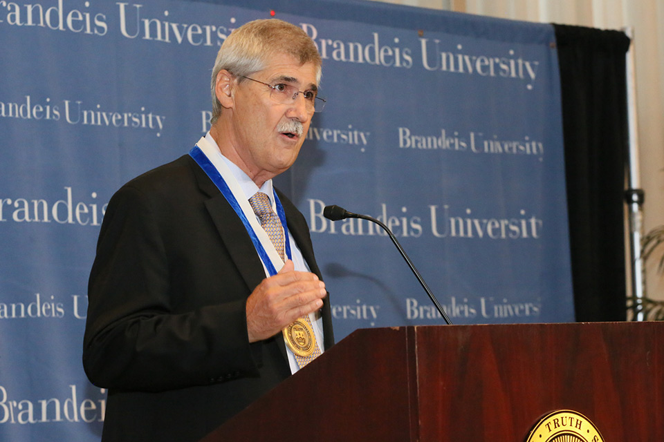 John Paul Lederach speaking at a podium, wearing the Gittler Prize medal