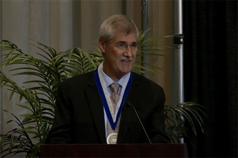 John Paul Lederach wearing the Gittler Prize medal speaking at a podium