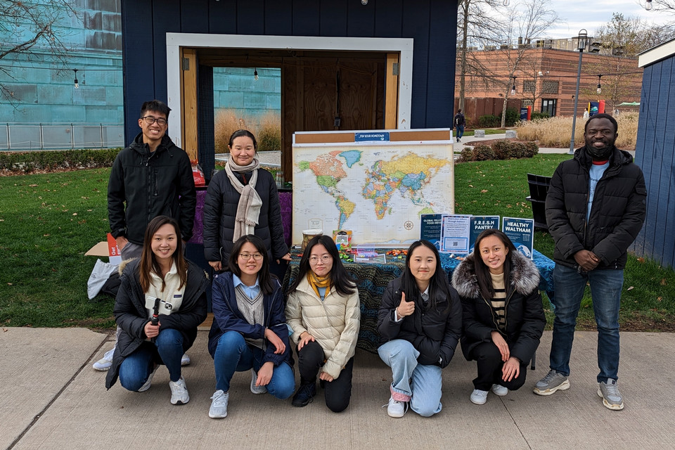 Global fellows smiling outside in front of a world map on the Brandeis campus. 
