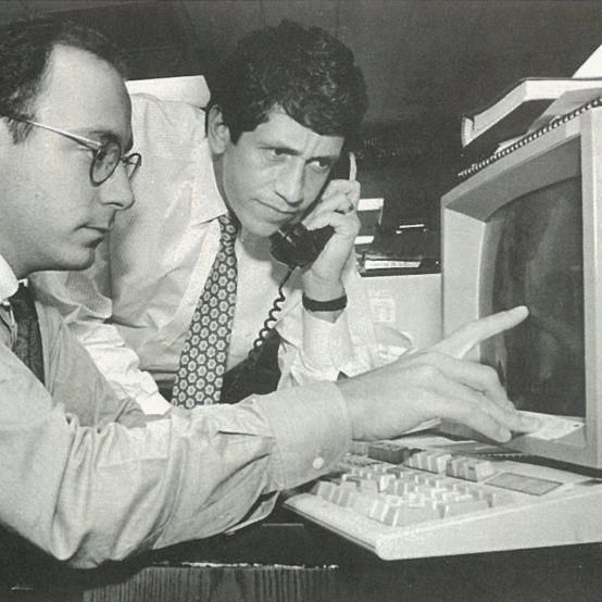 Two men doing work on an older computer.